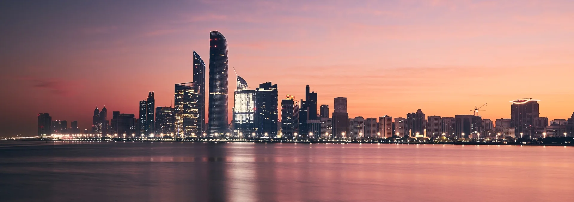 Abu Dhabi skyline at sunrise seen across the water, the sky in pink and orange