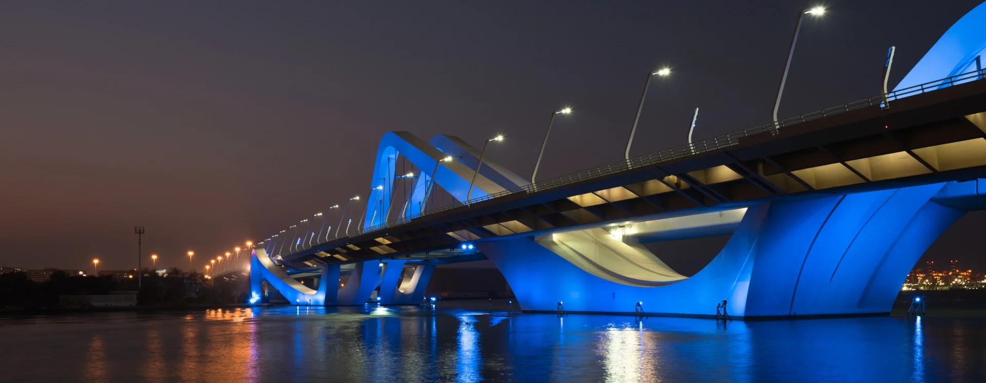 The Sheikh Zayed Bridge in Abu Dhabi at night, its arches lit in blue and mirrored in the water